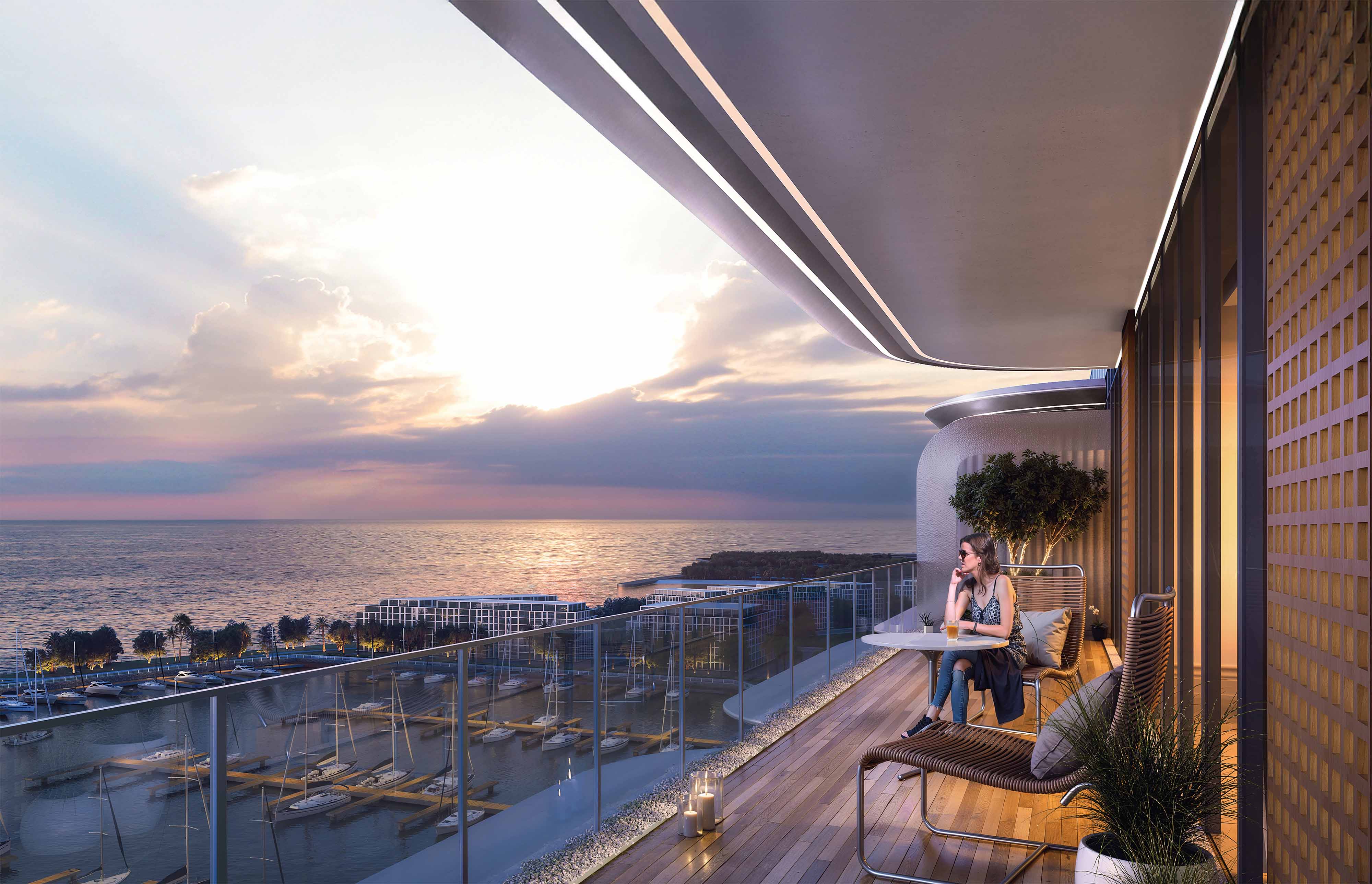 Cotier House 2 By Imtiaz A woman sitting on a balcony, enjoying a drink with a sea view at sunset, surrounded by modern furnishings.